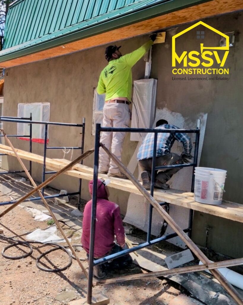 Construction workers applying stucco to a residential exterior wall using scaffolding
