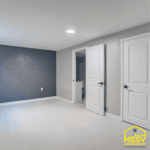 Finished basement renovation with gray accent wall, white doors, recessed lighting, and new flooring