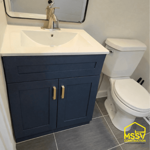 Modern bathroom vanity with navy cabinet, white sink, brass hardware, and gray tile floor