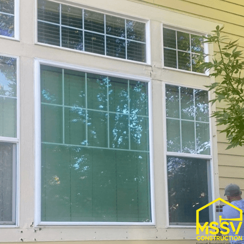 Worker repairing siding and trim around large residential windows