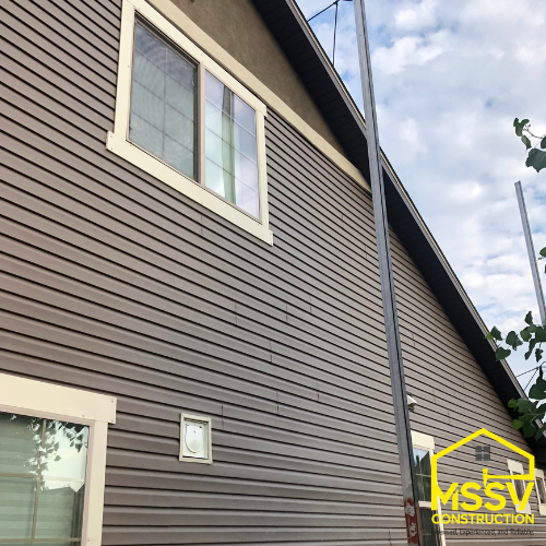 Two-story home with dark brown horizontal siding, white trimmed windows and exterior downspout