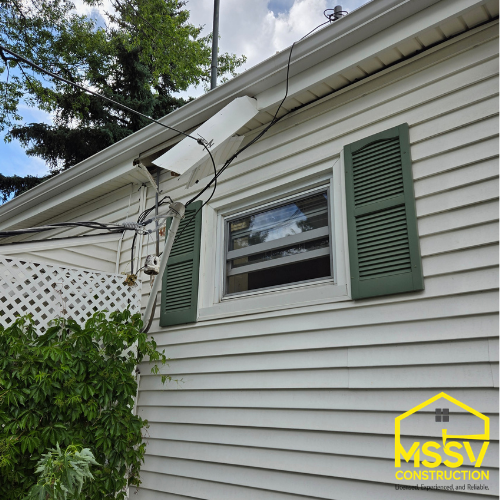 Residential home exterior with light colored vinyl siding, white window trim, and green shutters by MSSV Construction