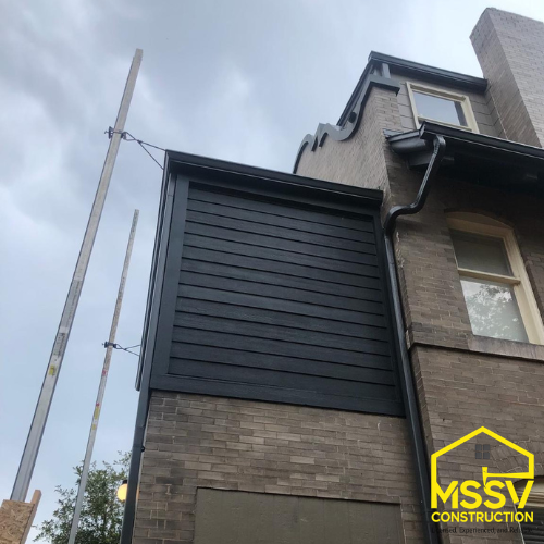 Upper residential exterior with dark siding panels, roofline and construction supports