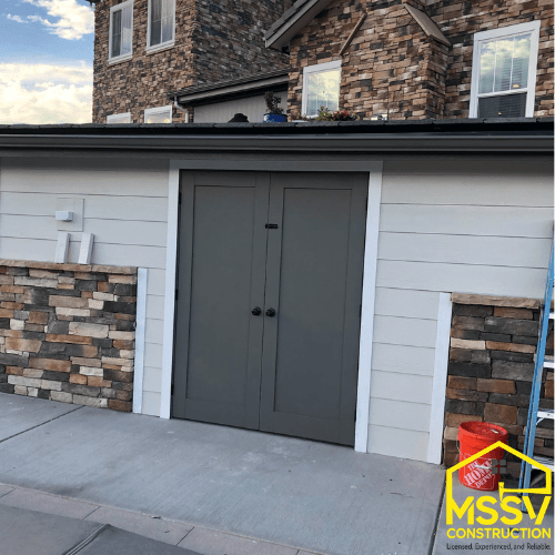 Custom outdoor shed enclosure with gray double doors, stone accents and white siding by MSSV Construction